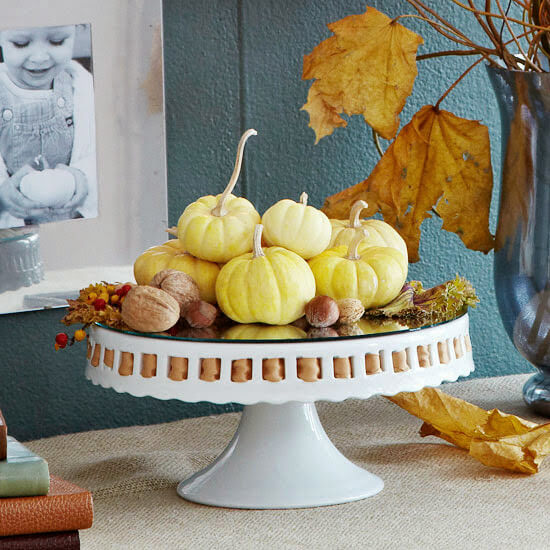 Mini pumpkins and other fall decor on a raised white cake stand