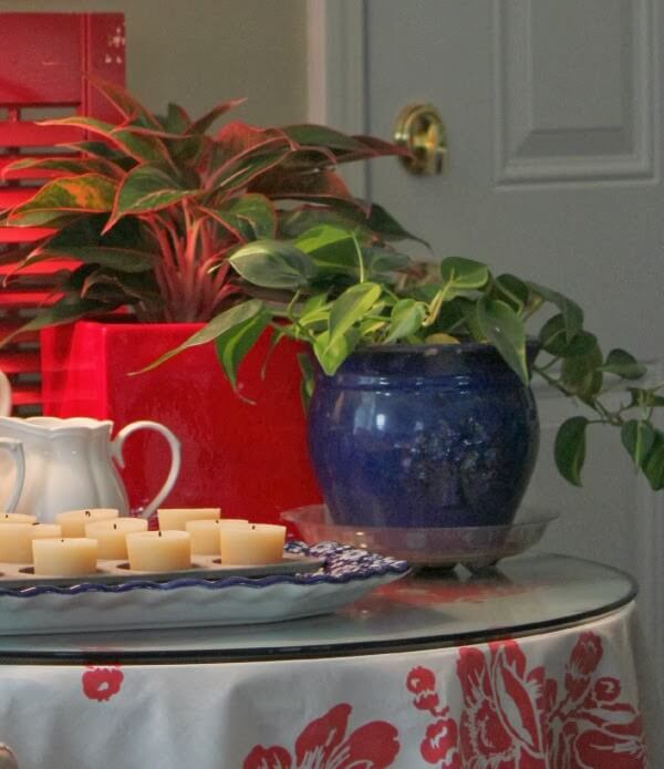 This vignette of votive candles in a muffin tin, a cobalt blue pot with philodendron, a white pitcher and a plant in a red pot are part of my house plant love