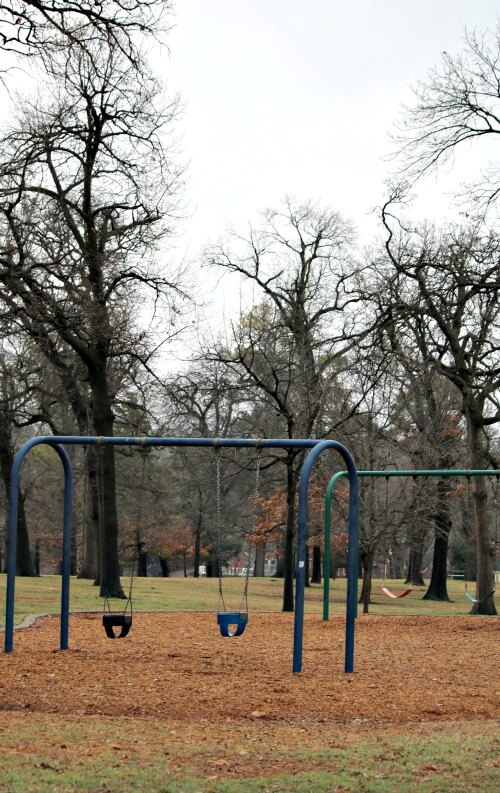 A park setting on a playground, where there is no one swinging on the swing set. An introvert in symbol.