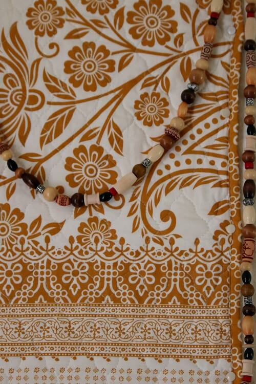The boho decor is hanging and draped on a caramel colored wall quilt.