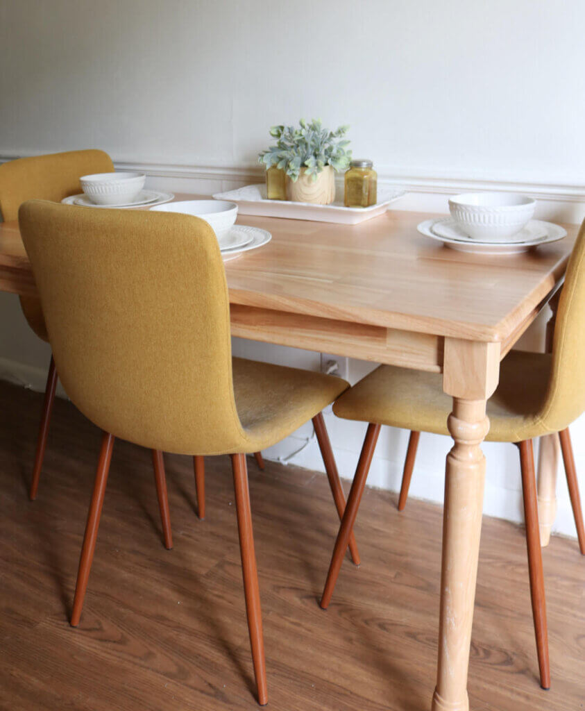 A light wood dining table with modern yellow-gold chairs and white dinnerware