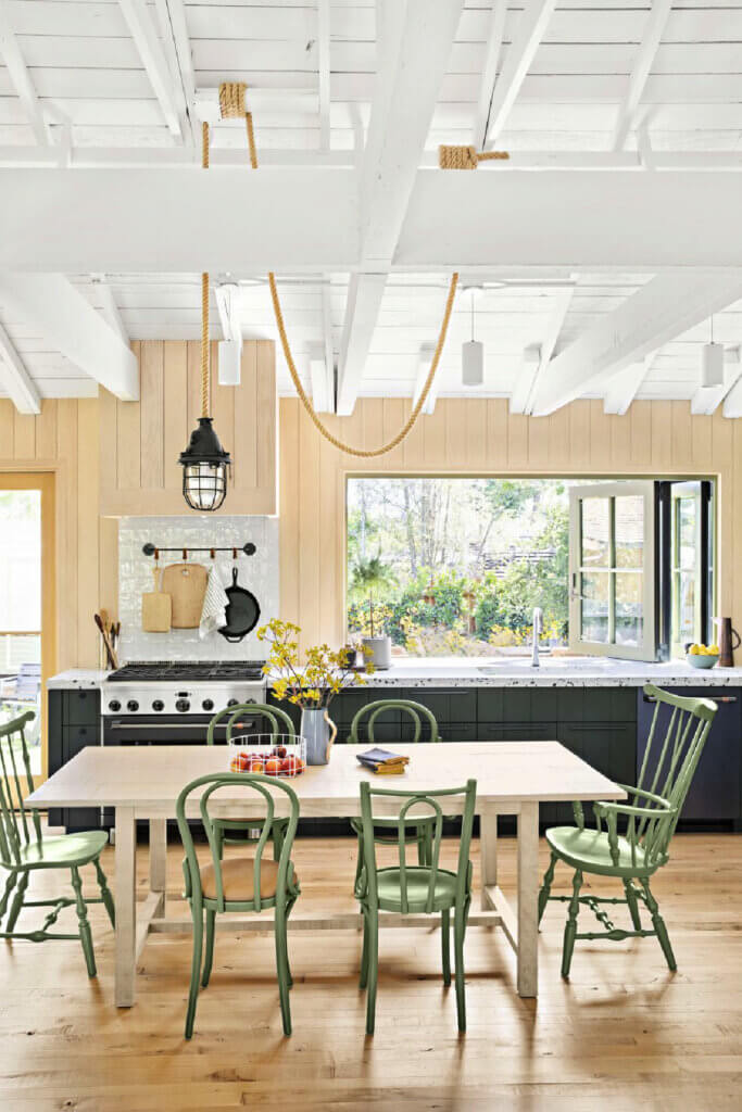 The kitchen has lots of natural light and a table with mismatched green chairs