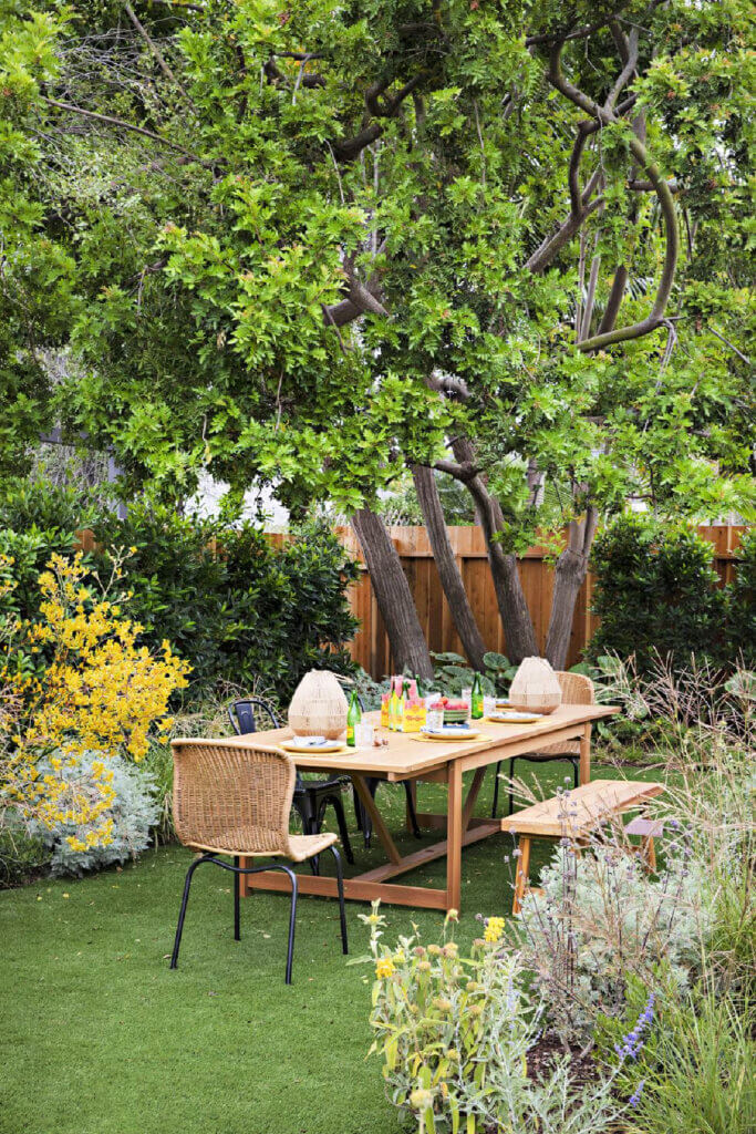 A grassy area has a table and chairs to dine outside of this dreamy 1950s Southern California Cottage