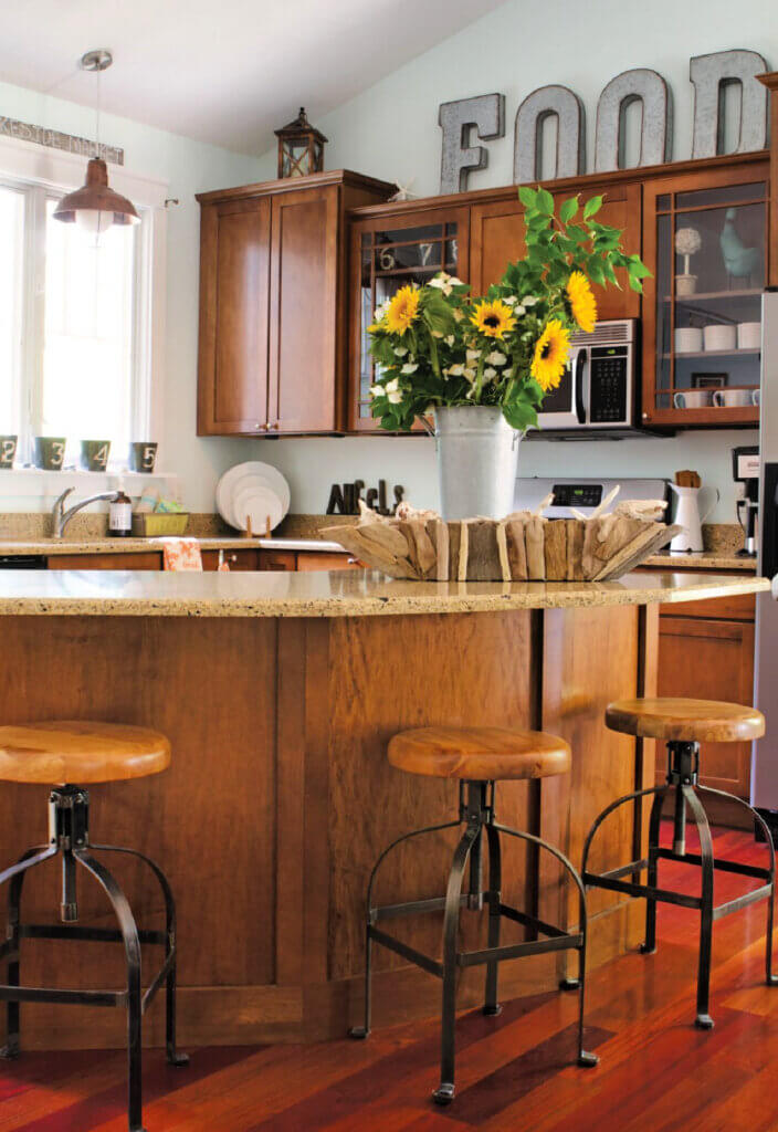 A kitchen with a bar and industrial style stools. A bucket of sunflowers is on top of the bar.