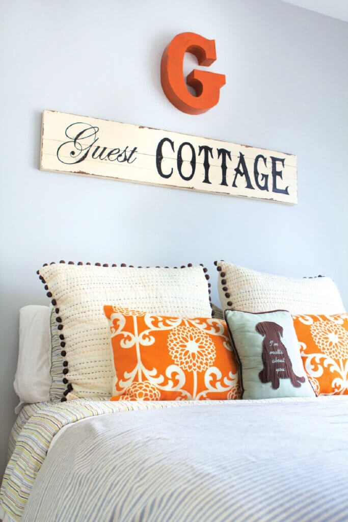 A bed with striped bedding and boho pillows and a sign that says Guest Cottage