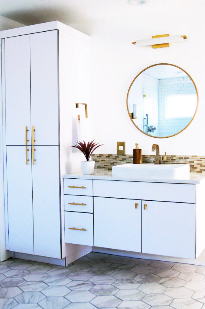 A bathroom with raised cabinetry, hexagonal tiles and gold hardware