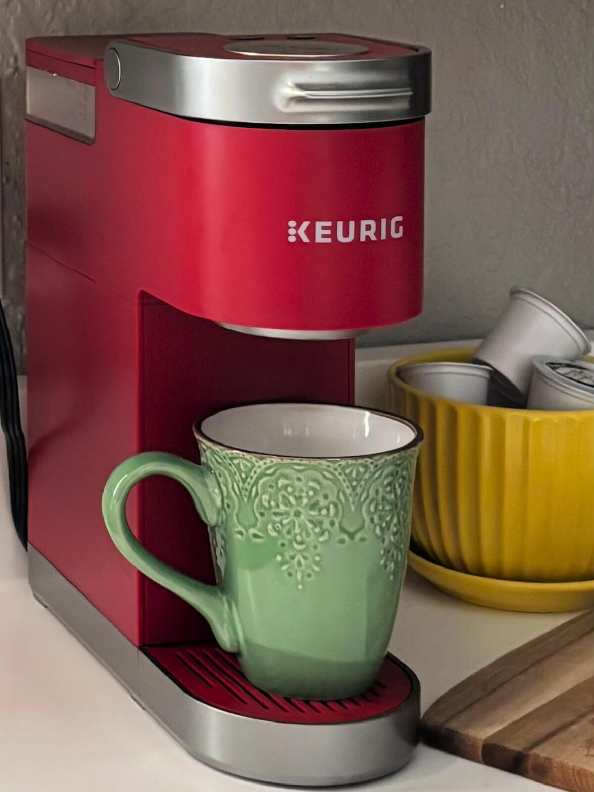 A red mini Keurig with a green coffee mug.