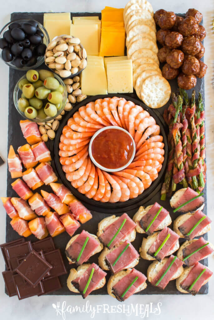 A meat and cheese board with shrimp and sauce in the center