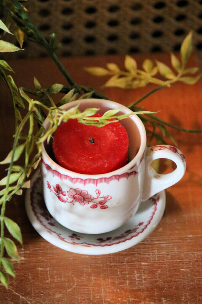 A little red and white mug and saucer with a red votive candle inside as Christmas decor