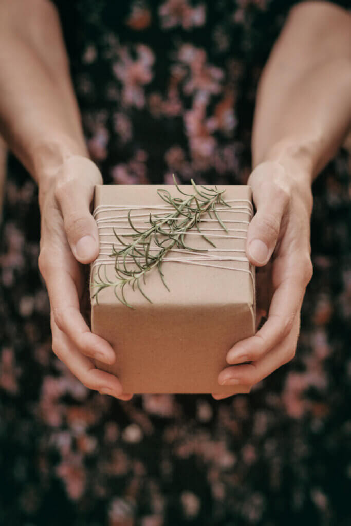A gift wrapped with plain paper and wrapped with twine and rosemary