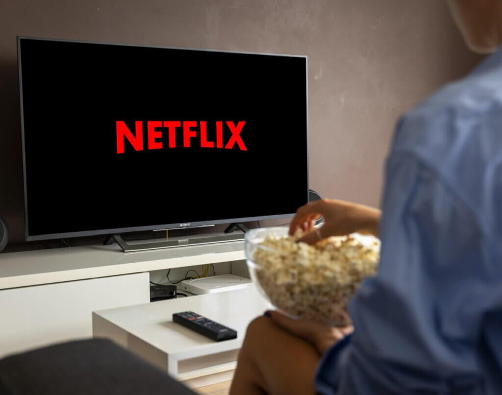 Photo of a man eating popcorn from a bowl while watching Netflix on his TV
