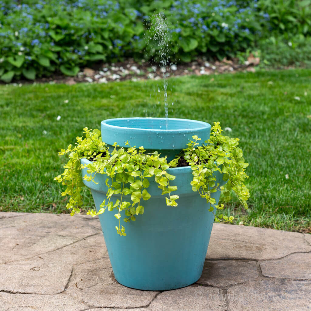 In how to create this diy water feature, the blogger painted two terra cotta pots and filled the bottom pot with dirt so she could add plants