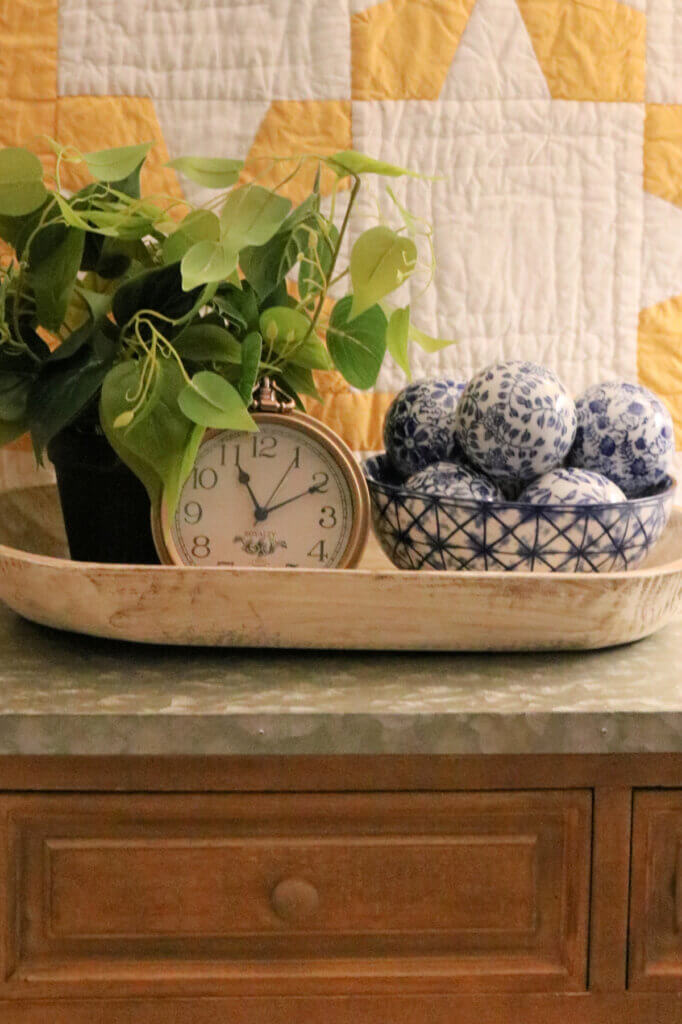 A dough bowl on a cupboard filled with decor