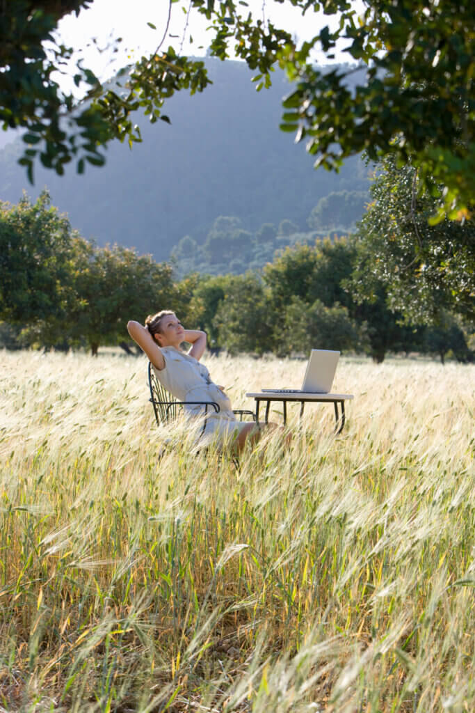 In settling into slow living, this shows a woman relaxing in a field of grass with her laptop in front of her.
