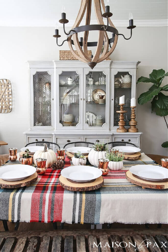 A plaid table setting with wood slices under the white plates for Thanksgiving.