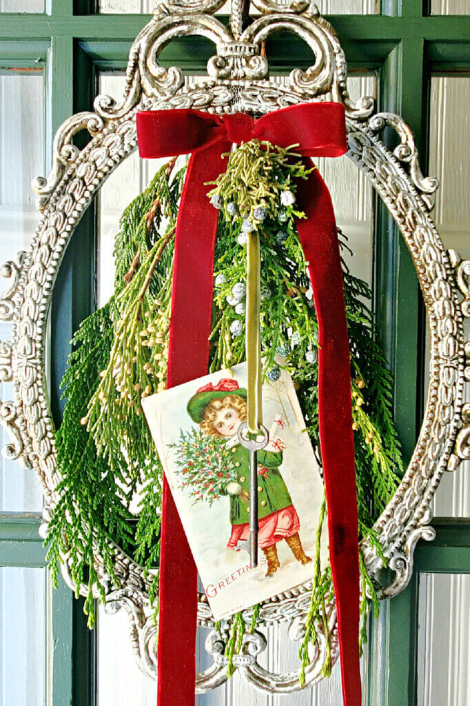 A holiday wreathe created with a picture frame, greenery, and a vintage card.