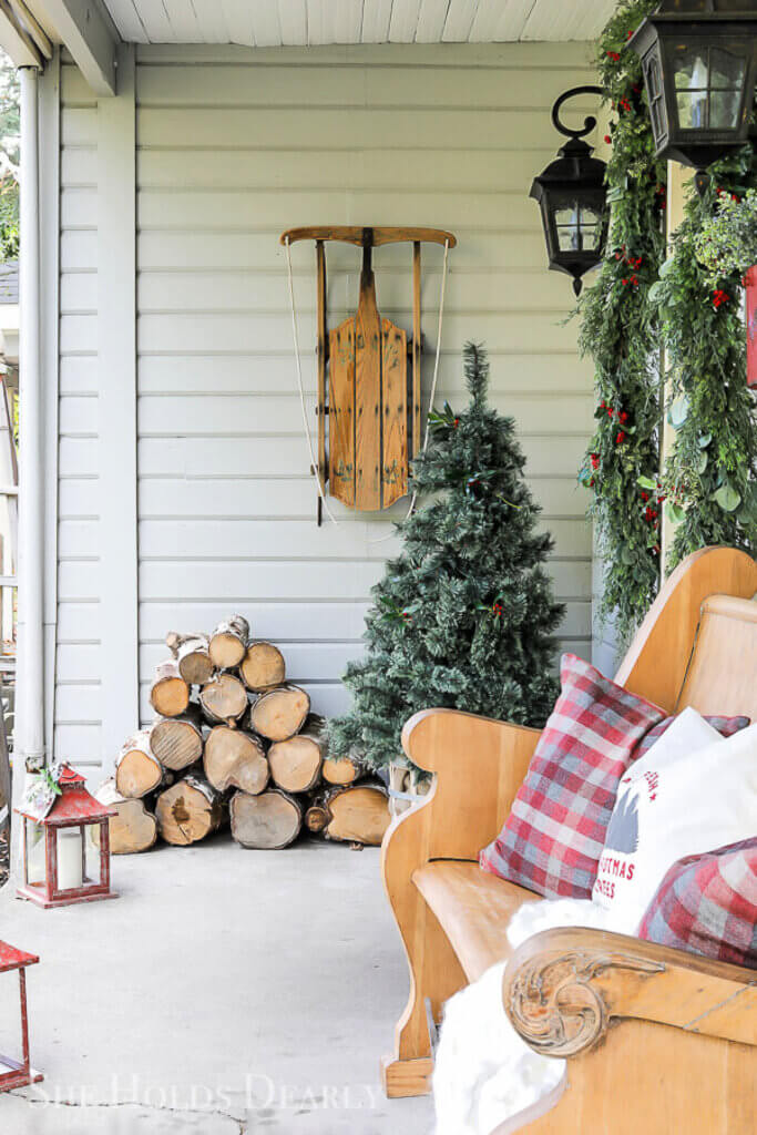 A porch with A Christmas tree, a sled hung on the wall, and greenery around the door.