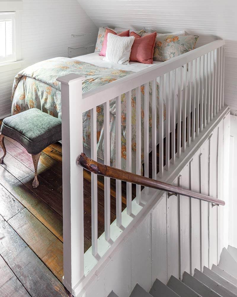 In A Charming Cottage In Tennessee, a bed sits in a small space next to the stairs.