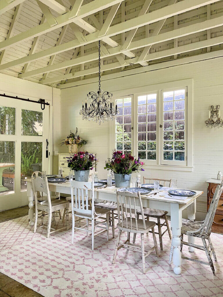 A rustic dining table and various chairs with buckets of flowers.