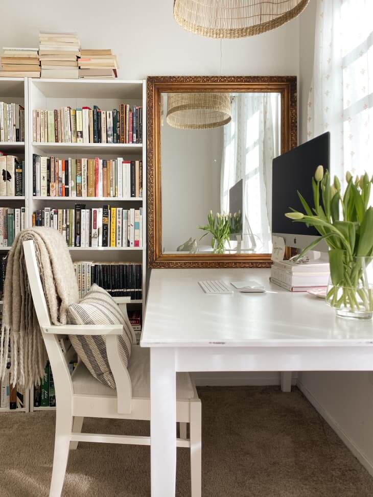 In What The Cozy Aesthetic Has Become, a desk in front of a large window with bookshelves to the side.