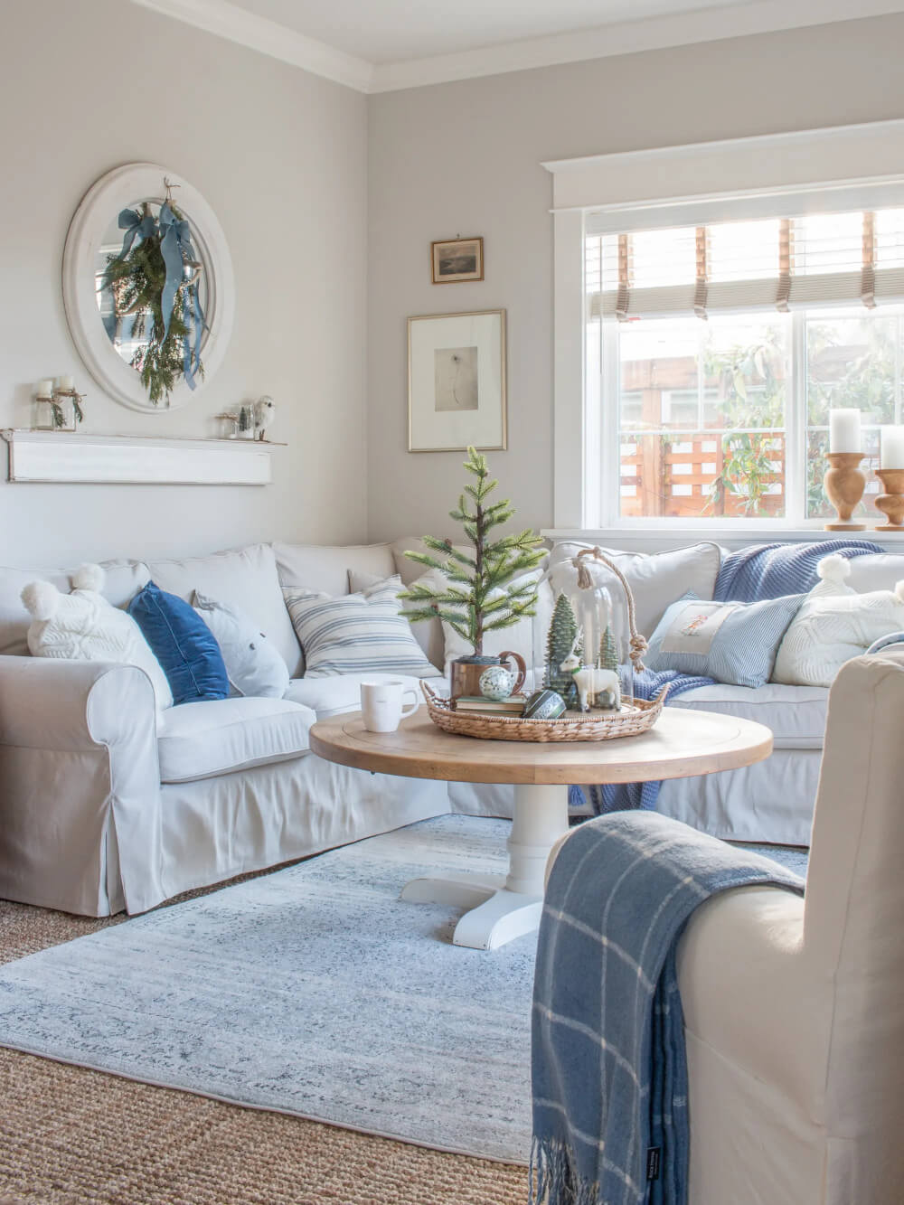 Blue and white pillows on a sectional surround a coffee table with a Christmas scene on top.