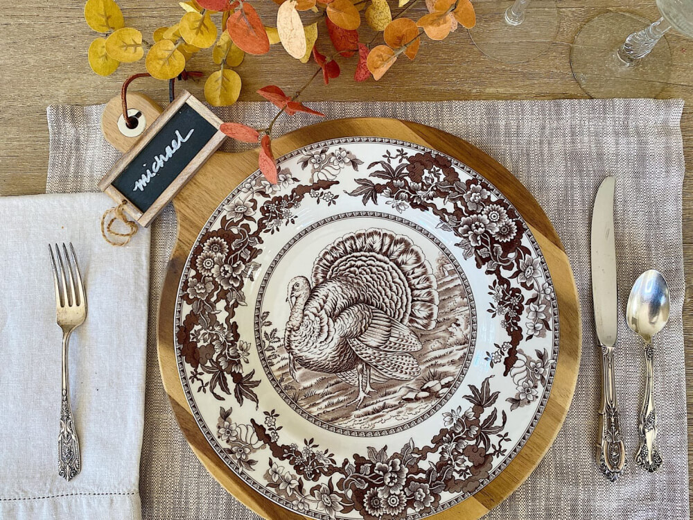 A brown transferware plate on a wooden charger at a place setting