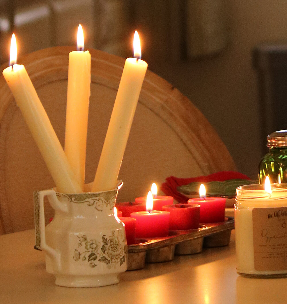 Tapered candles in a green transfer ware creamer next to various candles