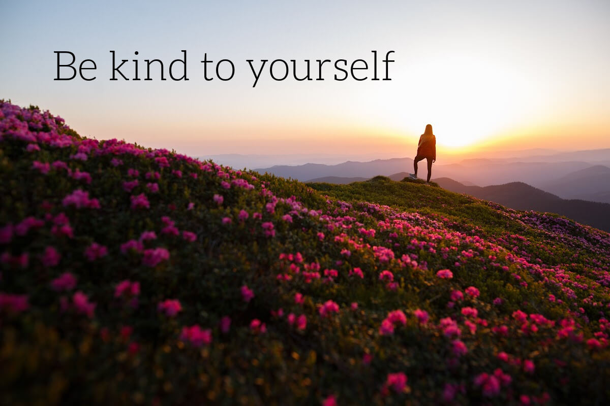 Woman standing on mountain: be kind .to yourself is what matters.