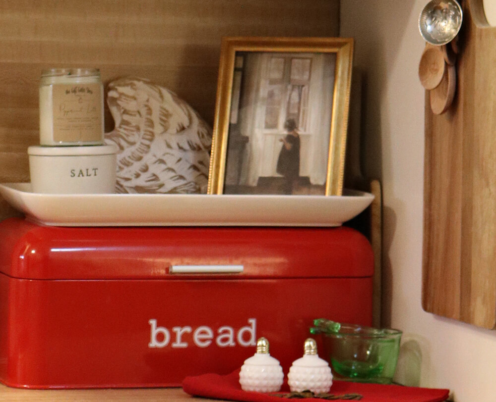 A red and white bread box with decor above it.