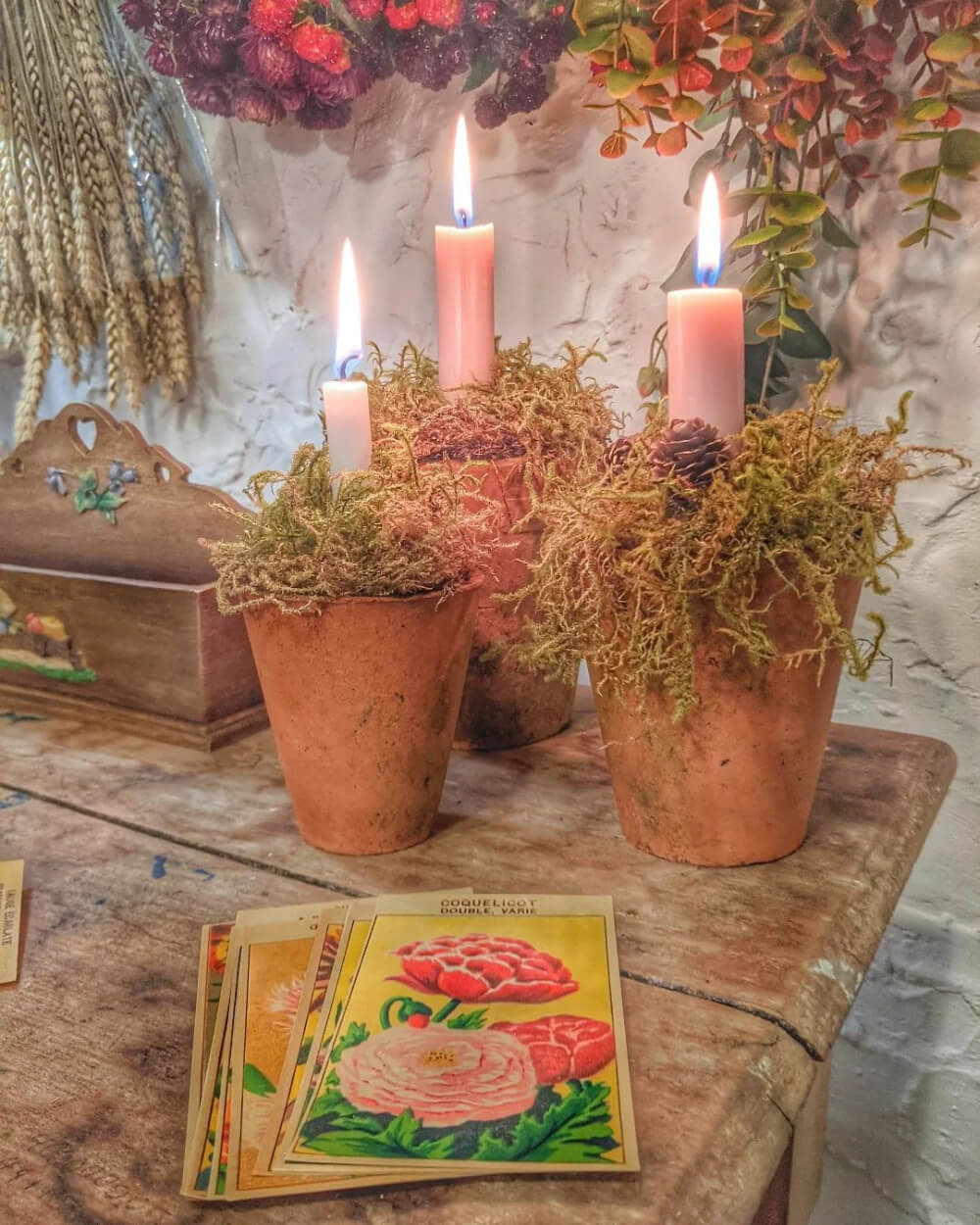 In The Love Of Home Files #19, three terra cotta pots with faux grass and candles. Vintage seed packets are on the table too.