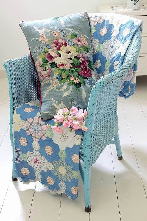 A blue wicker chair with a patchwork quilt and a floral pillow.