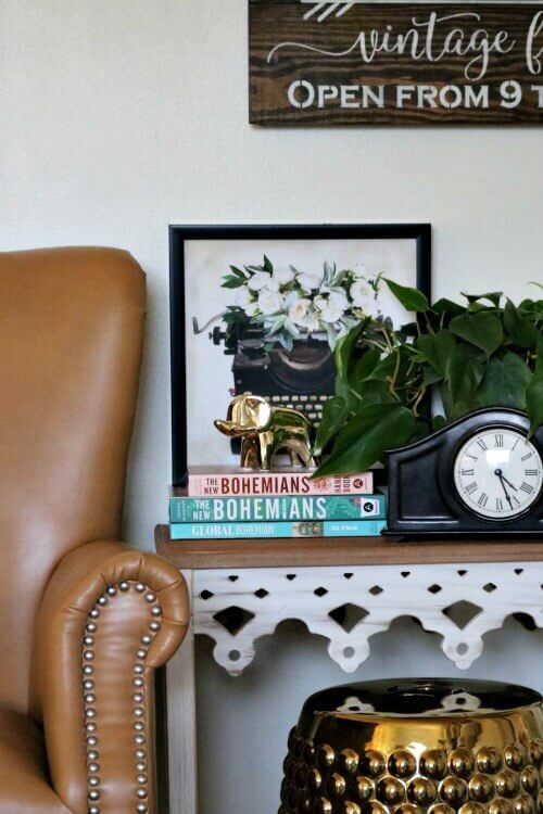 Admiring Decor Without Wanting to Redecorate, such as with this faux leather chair, white wooden side table with books and plants and clock. Gold garden stool underneath.