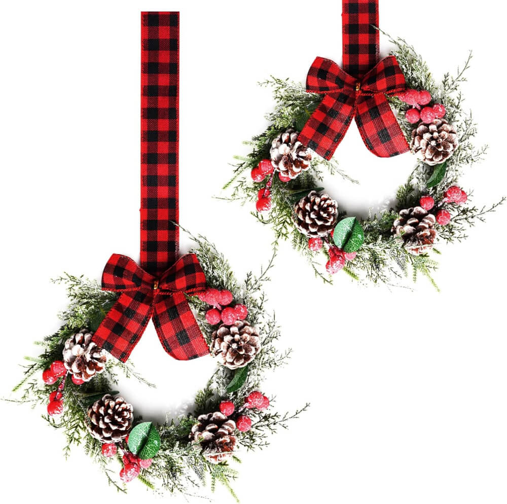 Wreaths with red berries and pine cones hung with red and black ribbon at Amazon.