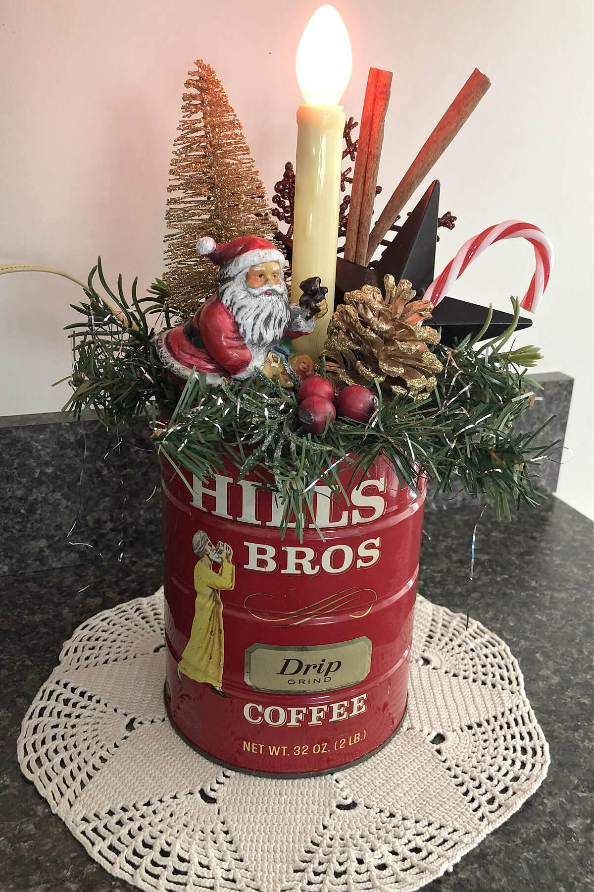 Hills Brothers vintage coffee can with Santa, gold pinecone, red berries, candy cane, greenery, star, bottle brush tree, and candle.