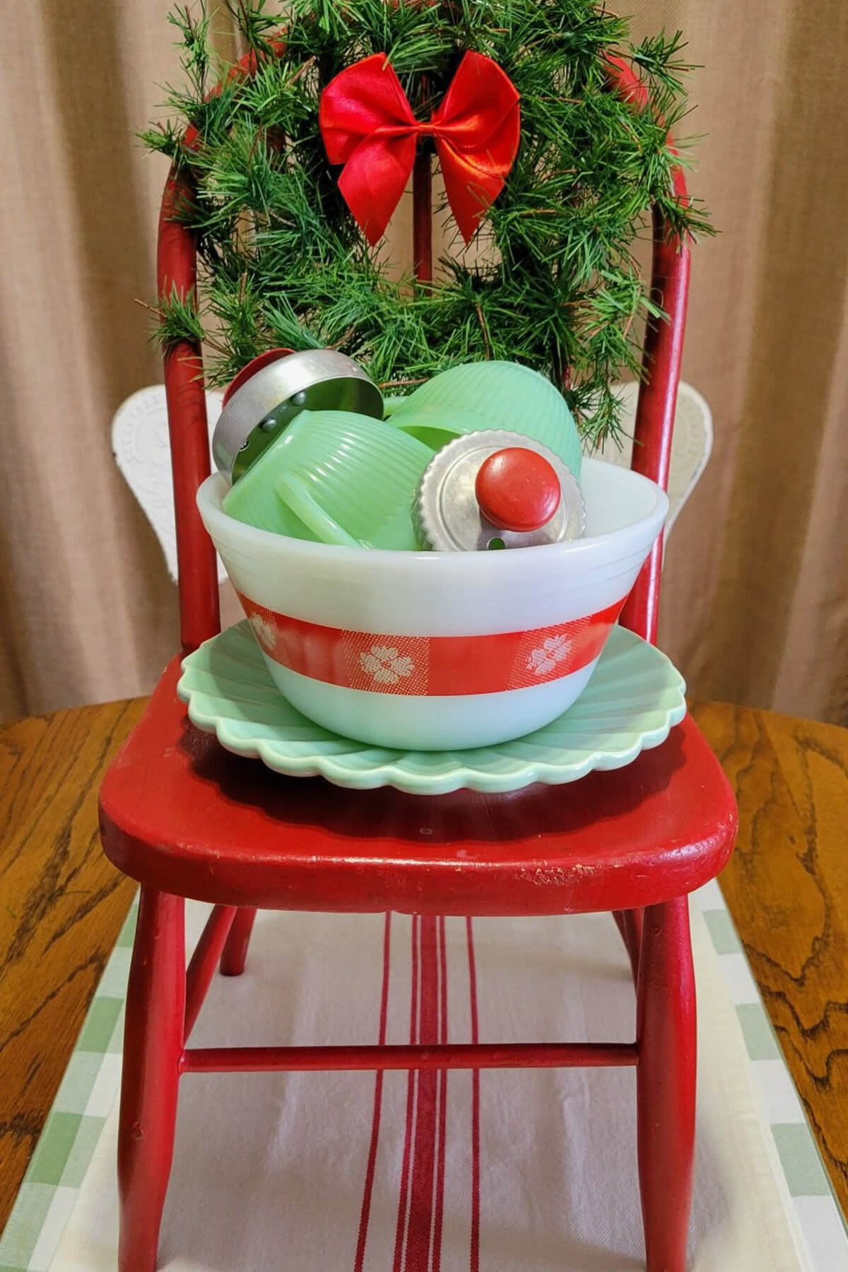 Budget-Friendly DIY holiday decorations is a red chair with a wreath and red bow. In the chair is a vintage red and white bowl holding Jadeite and cookie cutters.