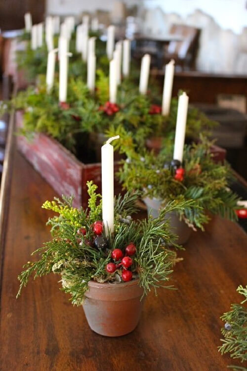 Budget-Friendly DIY holiday decorations of terracotta pots with red berries, greenery, and white taper candles.