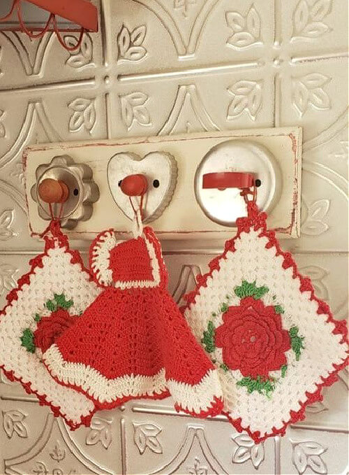 A small piece of wood with attached vintage cookie cutters, and crocheted kitchen items hanging from the cookie cutters.