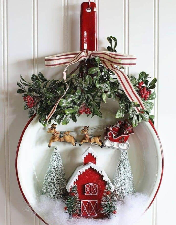 Red and white enamelware water dipper with miniature red barn, bottle brush trees, and Santa and his reindeer with tied ribbon and greenery.