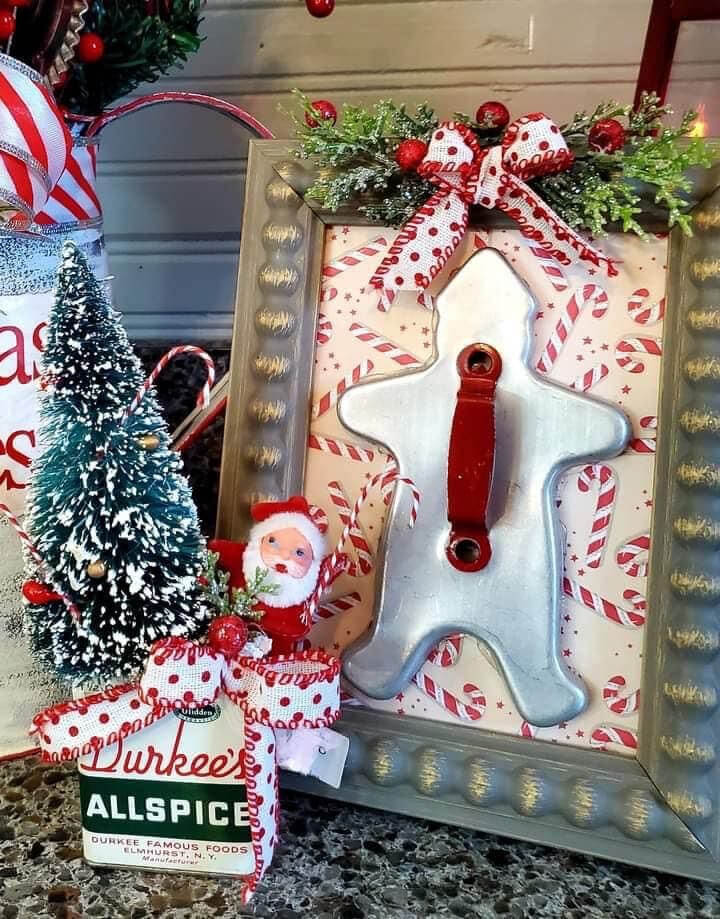 Budget-Friendly DIY holiday decorations with a framed gingerbread man cookie cutter, next to an allspice tin with a bottle brush tree, Santa, and a polka dotted red and white bow.