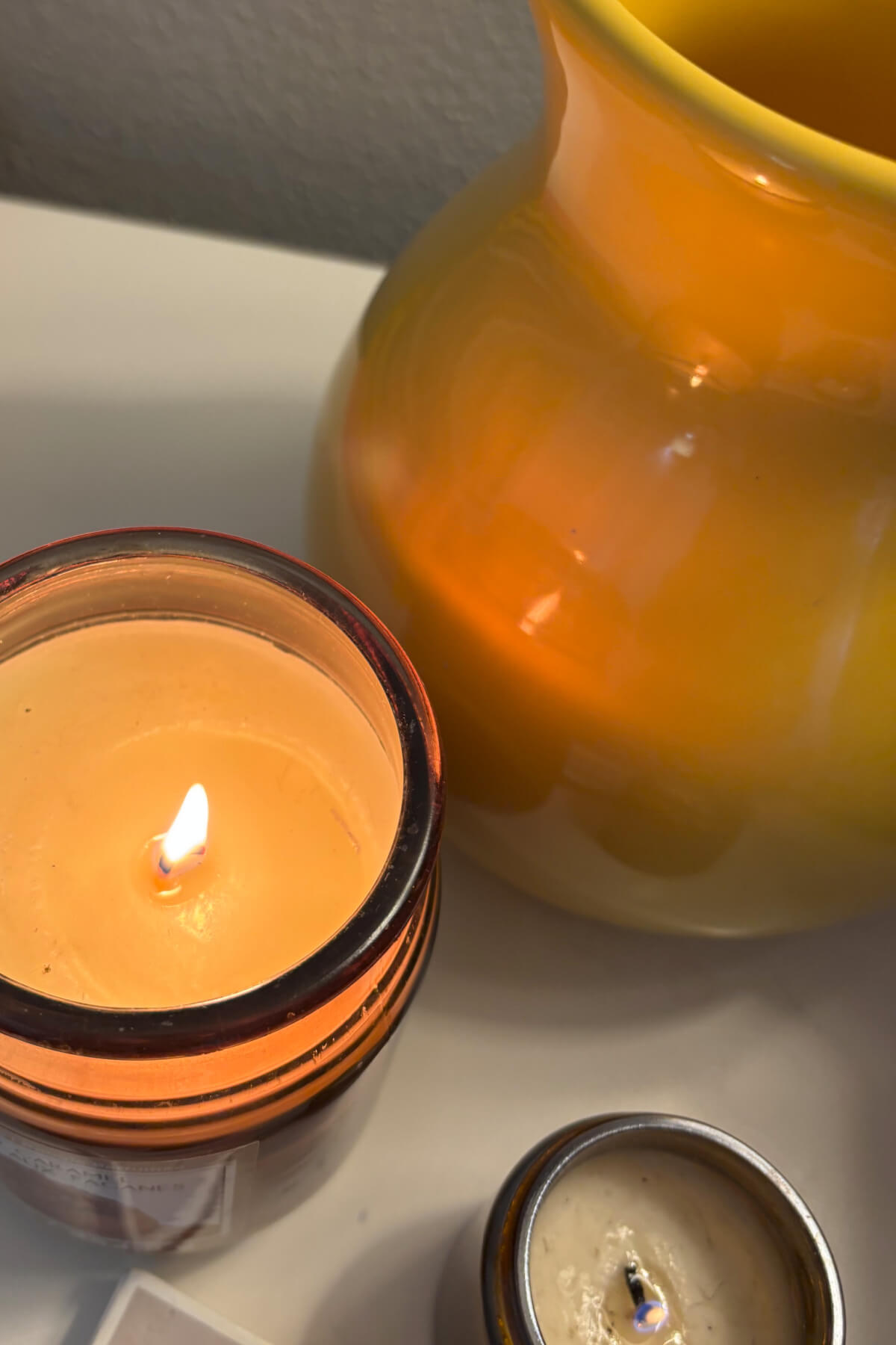 A close up photo of candles and a yellow pitcher.