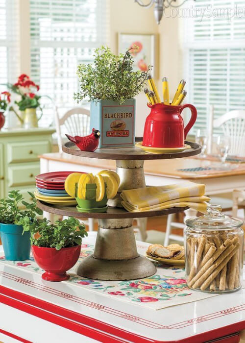 A red-and-white enamel table that is ideally suited for the 1950s era, with two vintage cake plates, a few pots of herbs, and cookies in a jar.