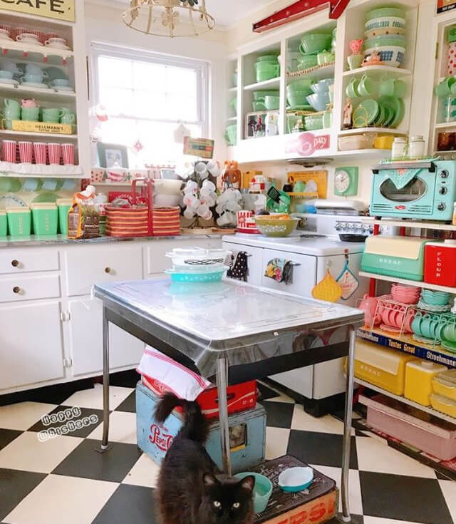 A black-and-white enamel table sits in the center of this kitschy, colorful kitchen. There is a Jadeite collection, vintage canisters, and a turquoise microwave.