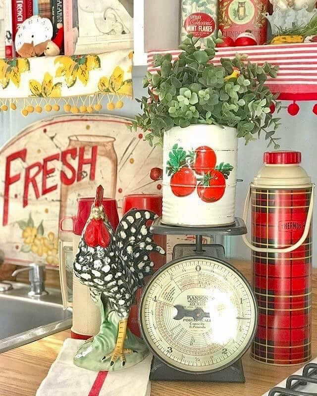 A rooster holds court next to vintage kitchen scales (plus a painted-tomato can on the front) and a plaid thermos. A red-and-white "Fresh" sign sits behind the sink.