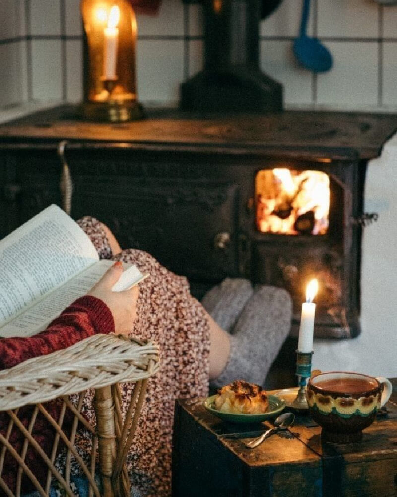 Sitting in front of the fire in a wicker chair with a book and a candle glowing.
