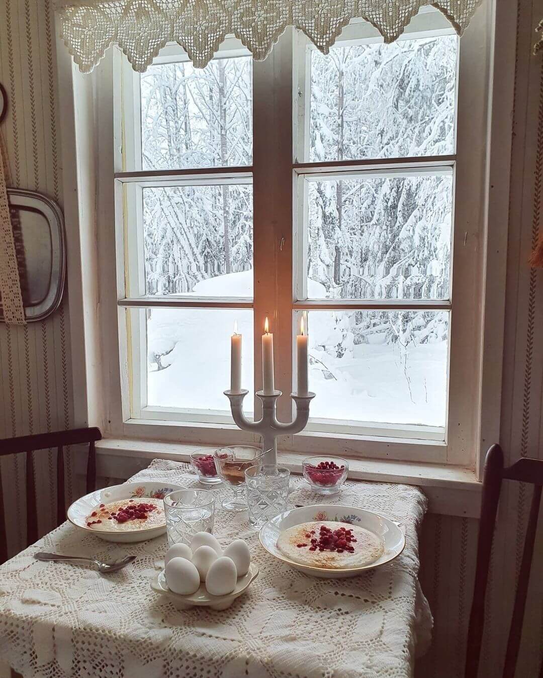 Sitting at a table next to the window where it snows outside, enjoying breakfast by candlelight.