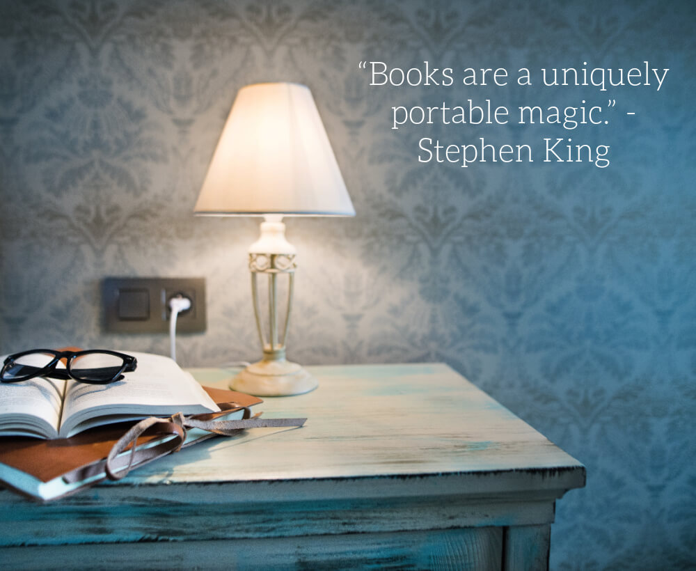 Image of lamp and open book on table with glasses and a quote about books.