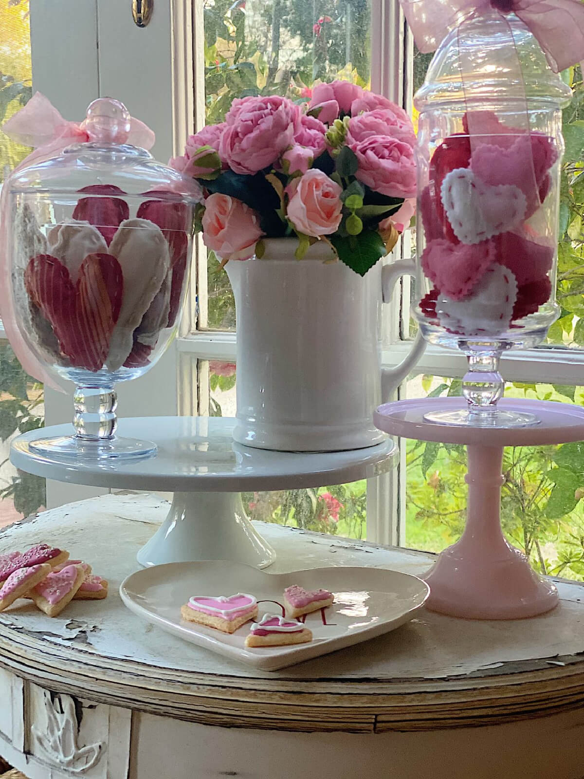 White pitcher with pink flowers, and clear glass cloches with stuffed hearts.