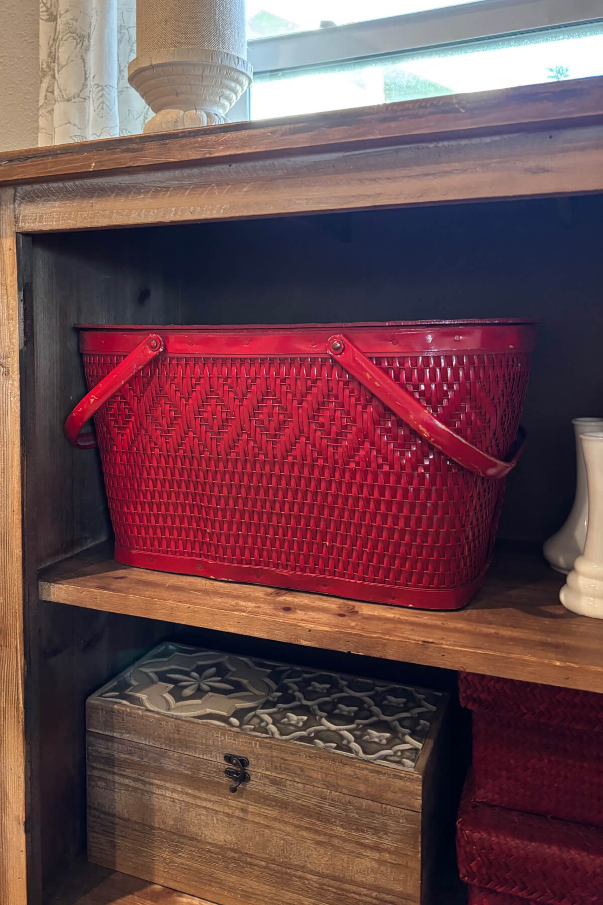 Red picnic basket, red woven storage baskets, and a wooden box in a shelved cupboard.