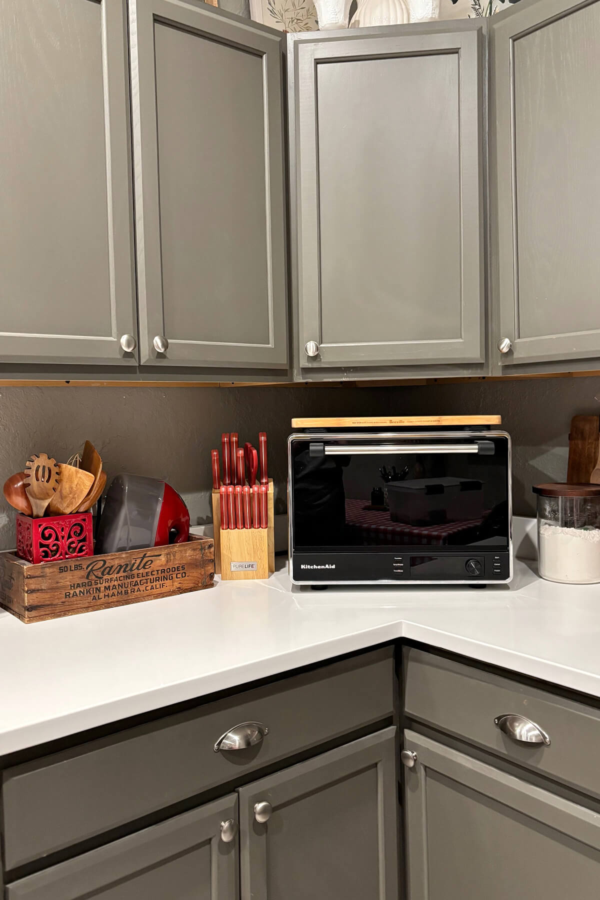 A red kitchen utensil holder and hand mixer stored in a vintage wooden box.