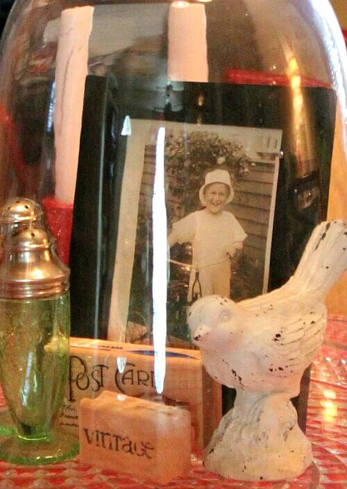 A glass cloche with a vintage framed photo, green salt and pepper shakers, a bird, and wooden stamps inside.